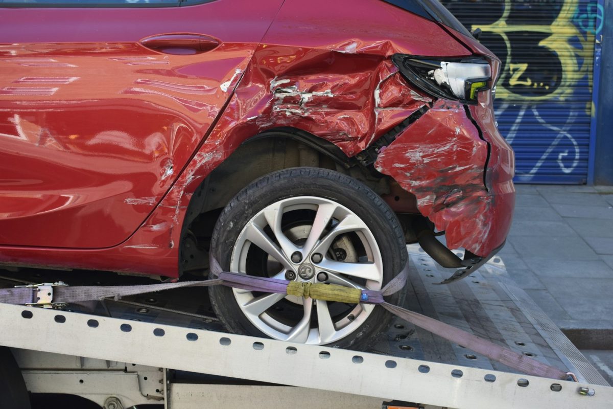 A damaged red car on a flatbed tow truck